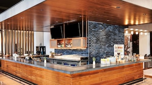 A modern bar area with a wooden counter, a brick accent wall, and a flat-screen TV mounted above the bar. - Hyatt Centric Downtown Denver (Denver)