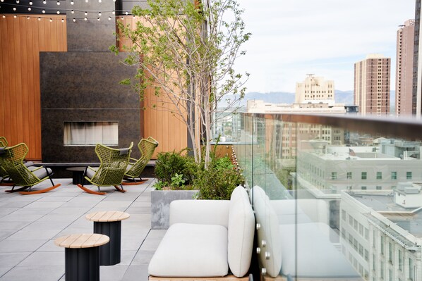 A rooftop terrace with seating, a fire pit, and a view of the cityscape.