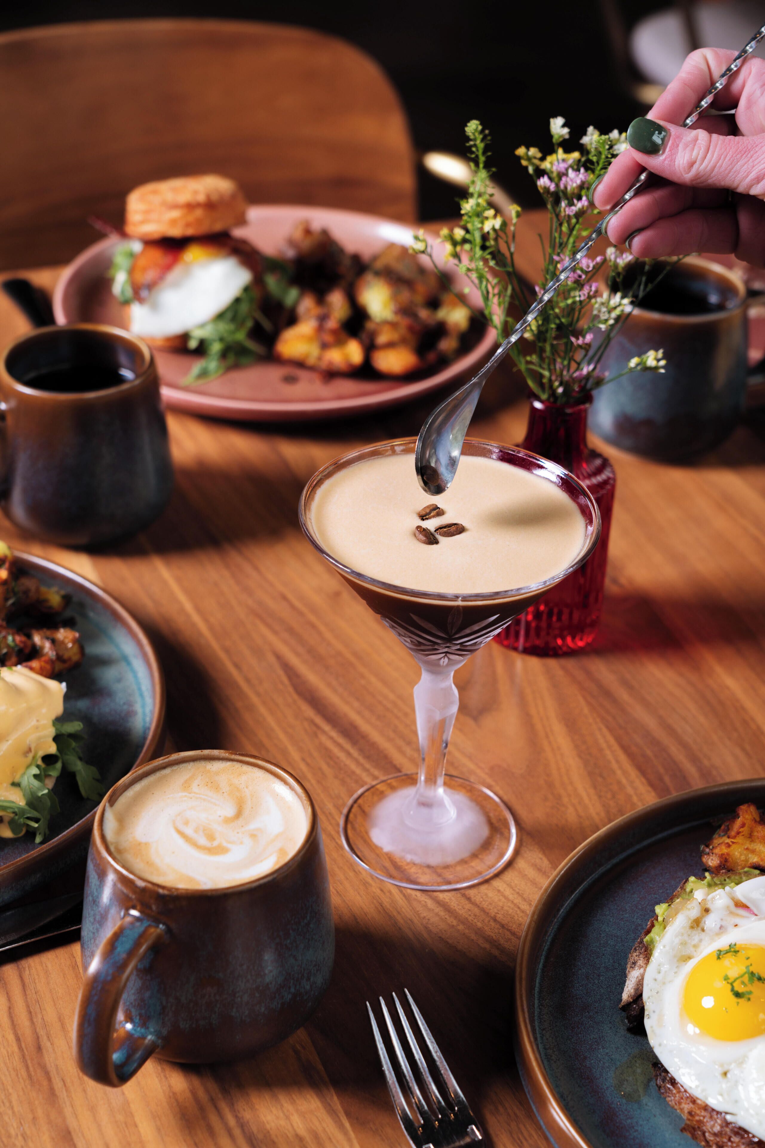 A dining table with a martini glass, a coffee mug, and plates of food.