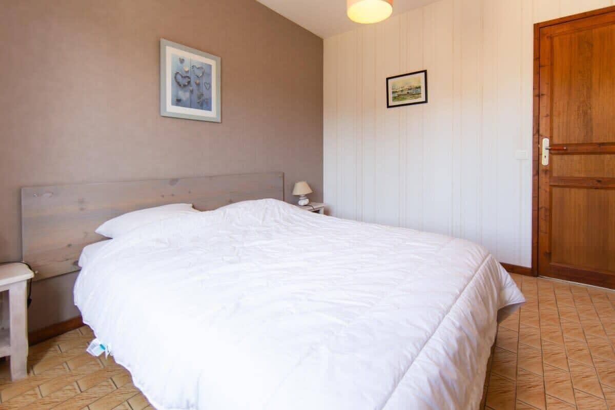 A bedroom with a wooden headboard, a white bedspread, a bedside table with a lamp, and a wooden door.