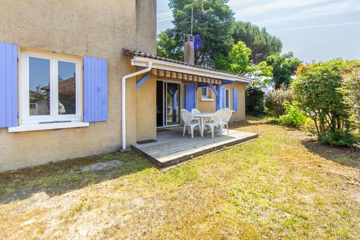 A house with a wooden deck, a patio with white plastic chairs, and a small table.