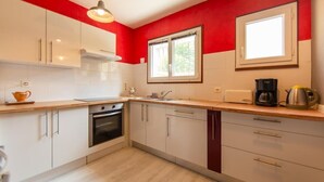 Een moderne keuken met witte kasten, een rode accentmuur, een raam en een koffiezetapparaat.