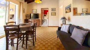 Een woonkamer met een eettafel, houten stoelen, een bank en een televisie.