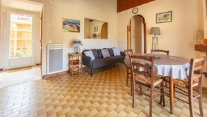 Een kamer met een houten vloer, een eettafel met stoelen, een bank, een lamp en een klok aan de muur.