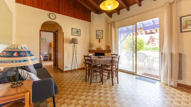 Een eetgedeelte met een houten tafel en stoelen, een lamp en uitzicht op de omgeving door een glazen deur.