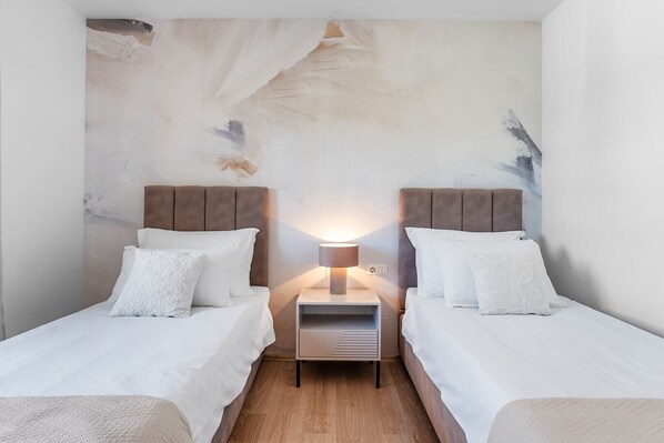 A hotel room with two beds, a nightstand with a lamp, and a textured wall.