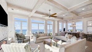 A spacious living room with a large window overlooking the sea, a fireplace, and a ceiling fan. - Luxe group-friendly beachfront escape with pool, hot tub, & expansive Gulf views (West Panama City Beach)
