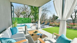 A modern outdoor living area with a pool, lounge chairs, and a wooden table. - Modern Villa Barcolana with a swimming pool (Baderna)