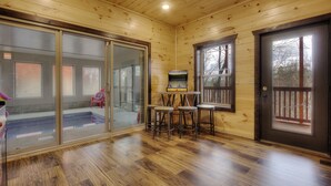 A wooden cabin interior with a sliding glass door leading to a balcony, a small table with stools, and a fireplace. - 🏊 OUTDOOR & 👙 INDOOR PRIVATE POOL CABIN | 🎮 Game Room 🕹️ (Sevierville)