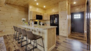 A wooden cabin-style kitchen with a central island, bar stools, a refrigerator, and a microwave. - 🏊 OUTDOOR & 👙 INDOOR PRIVATE POOL CABIN | 🎮 Game Room 🕹️ (Sevierville)