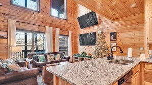 A cozy cabin interior with a wooden interior, a large kitchen island, a dining area with a couch, and a Christmas tree. - 🏊 OUTDOOR & 👙 INDOOR PRIVATE POOL CABIN | 🎮 Game Room 🕹️ (Sevierville)