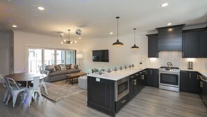 Una cocina moderna con una isla central, muebles oscuros, electrodomésticos de acero inoxidable e iluminación colgante.