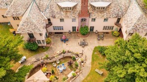 A large, multi-story building with a symmetrical facade, stone roof, and a central courtyard with outdoor seating.