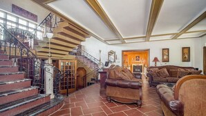 A spacious living area with a grand staircase, leather sofas, and a fireplace.