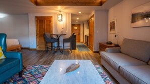 Un salon comprenant un canapé, une table basse ornée d’un motif en forme de feuille, un fauteuil bleu et un coin repas avec des chaises et une table.