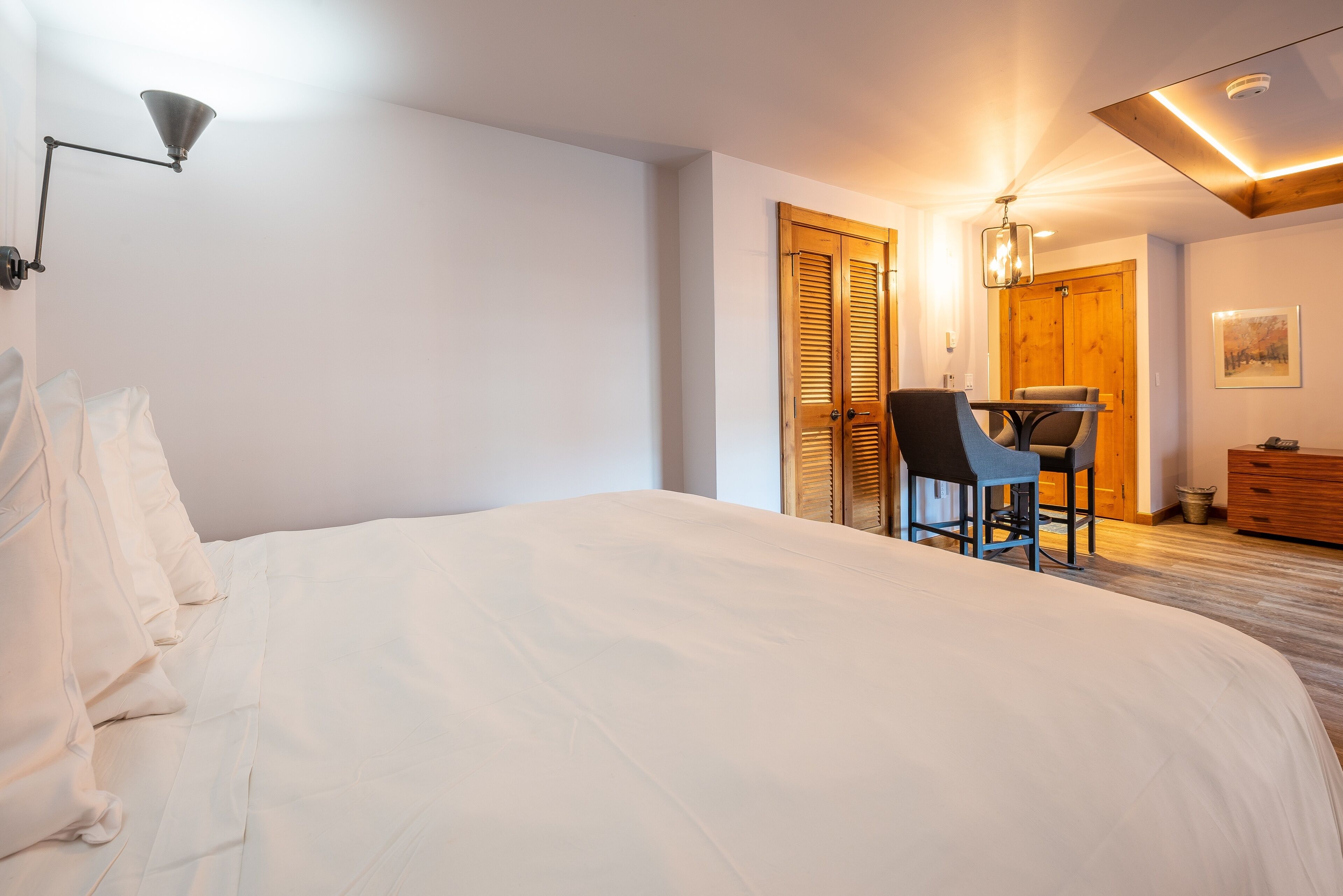 A bedroom with a large bed, a desk with a chair, and a wooden wardrobe.