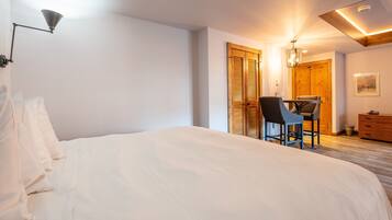 A bedroom with a large bed, a desk with a chair, and a wooden wardrobe.