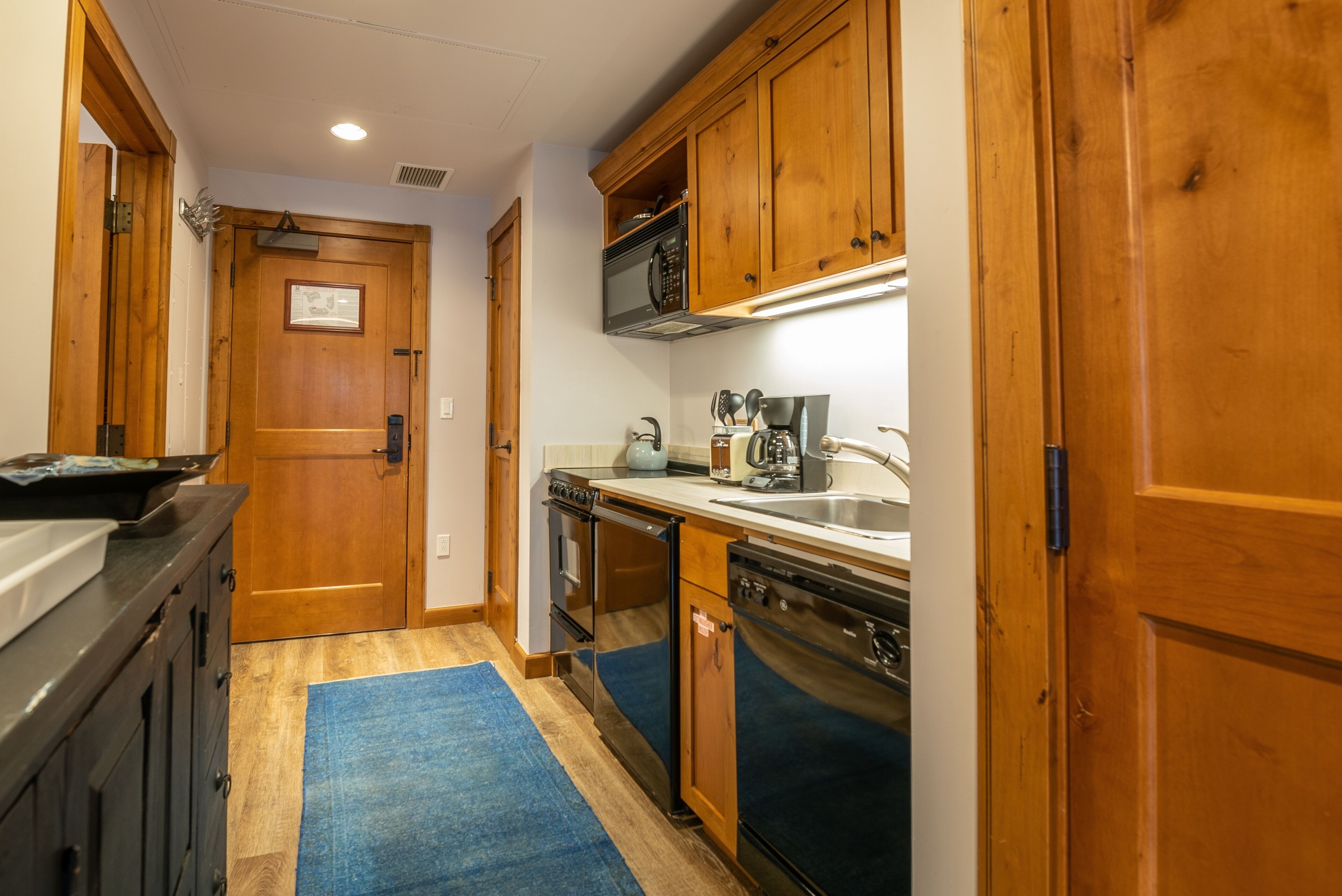 A compact kitchen with wooden cabinets, a stainless steel dishwasher, and a built-in oven.