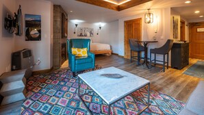 Une pièce confortable avec un lit, un fauteuil bleu, une petite table et un tapis coloré.