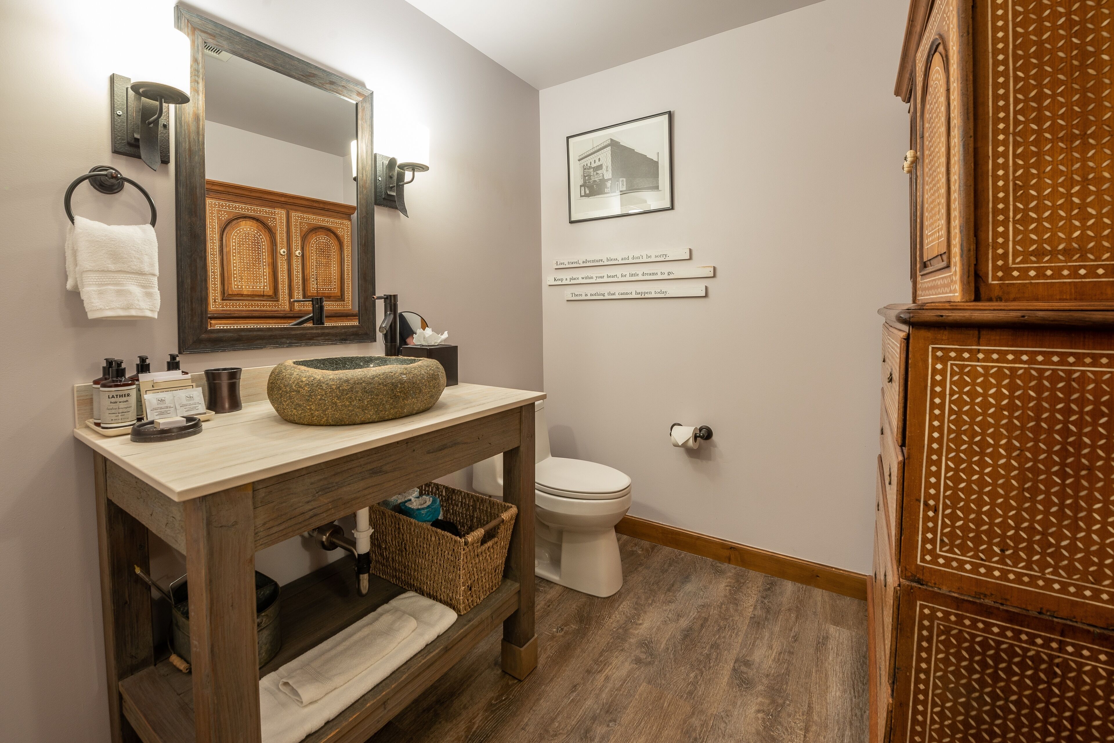 A bathroom with a wooden vanity, a large mirror, a white toilet, and a decorative cabinet.