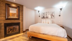 Une chambre à coucher avec un grand lit, une tête de lit en bois, une cheminée et deux lampes fixées au mur.