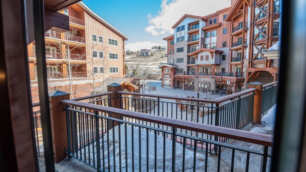 Une vue depuis un balcon donnant sur une station de ski, avec ses bâtiments en bois et le sol recouvert de neige.