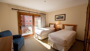 A hotel room with two beds, a sofa, a wooden desk, a lamp, and a view of a building through a sliding door. - Spacious 3 Bedroom Condo with Balcony in Mountaineer Square 3 Condo - No Cleaning Fee! by RedAwning (Crested Butte)