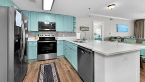 A modern kitchen with teal cabinets, stainless steel appliances, and a large island.