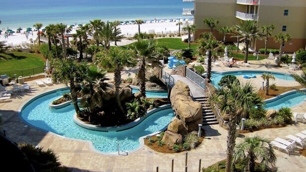 A resort with a pool area, palm trees, and a view of the beach.
