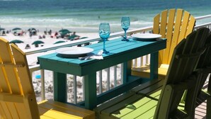 A table with two blue glasses and plates, set against a beach view.