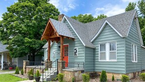 Une maison à deux étages avec un porche, une porte rouge et le numéro « 305 » sur la façade.