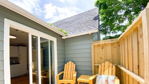 Une terrasse avec des chaises et une table en bois, une porte-fenêtre coulissante donnant sur une cuisine et une clôture en bois.