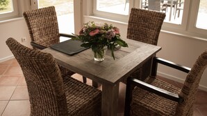 A dining table with wicker chairs, a laptop, and a vase of flowers. - Das Altenteil (Stoltebuell)