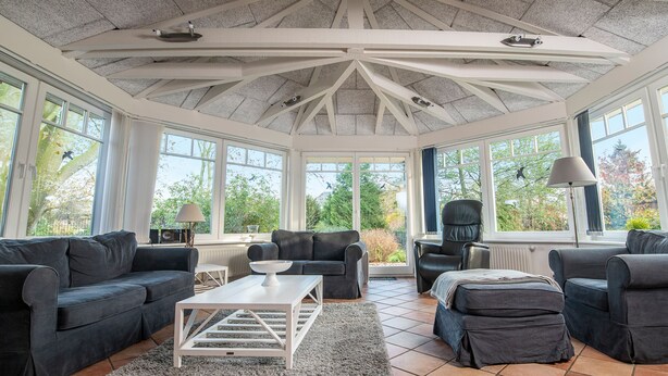 A sunroom with a high ceiling, large windows, and a cozy seating area with sofas and a coffee table. - Das Backhaus 2 (Stoltebuell)