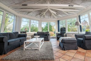 A sunroom with a high ceiling, large windows, and a cozy seating area with sofas and a coffee table. - Das Backhaus 2 (Stoltebuell)