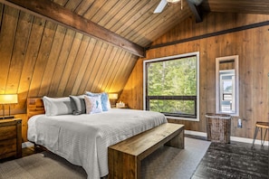 Un dormitorio con una cama grande, vigas de madera en el techo, una ventana con persianas, una mesita de noche y un banco.