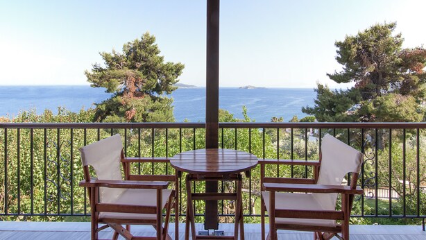 A balcony with a wooden table and two chairs, overlooking a scenic view of the sea and distant islands. - Olga Villa (Skiathos)