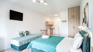 A bedroom with two beds, a TV, a kitchenette, and a wardrobe. - Olga Villa (Skiathos)