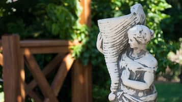 A statue of a figure holding a large object, set against a wooden fence and greenery.