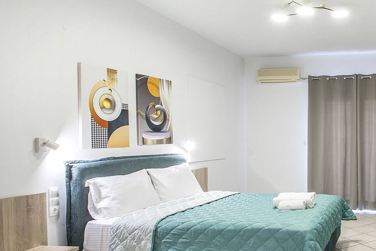 Una habitación de hotel moderna con cama, mesita de noche, aire acondicionado de pared y arte abstracto en la pared.