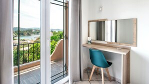A room with a balcony, a desk with a chair, a large mirror, and a view of a body of water and greenery. - Olga Villa (Skiathos)