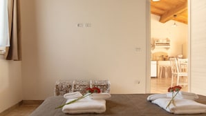 Ein Schlafzimmer mit einem Bett, einer kleinen Kommode und Blick in einen Essbereich.