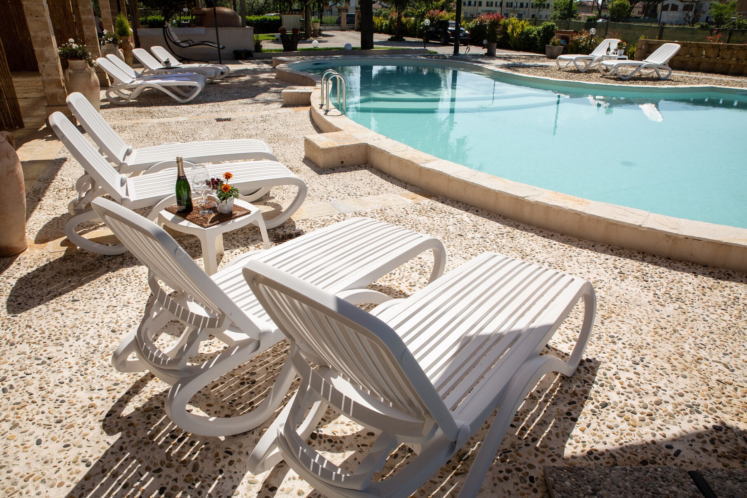 A poolside area with white lounge chairs and a table with a bottle and flowers.