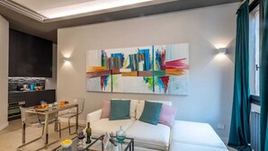 A modern living room with a white sofa, a glass coffee table, and a colorful abstract painting on the wall. - Sweett | Duomo 2A - Two Bedroom Apartment, Sleeps 4 (Milano)