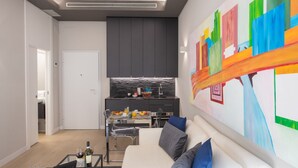 Un salon moderne avec un canapé blanc, une table basse en verre et un tableau abstrait aux couleurs vives accroché au mur.