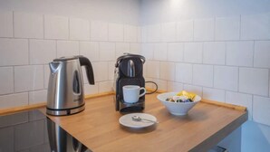 Une petite cuisine équipée d’une bouilloire, d’une machine à café, d’une tasse, d’un bol contenant de la nourriture et d’une assiette avec une cuillère.