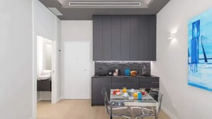Een moderne keuken met donkere kastjes, een marmeren spatwand en een eethoek met een glazen tafel en stoelen.