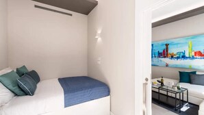 Een kleine, moderne slaapkamer met een eenpersoonsbed, een schilderij aan de muur en een deur naar een woongedeelte.