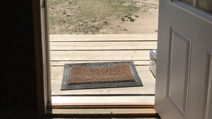 A view through a door of a grassy yard with a wooden deck and a welcome mat.