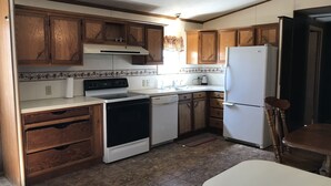 A compact kitchen with wooden cabinets, a stove, a dishwasher, and a refrigerator.